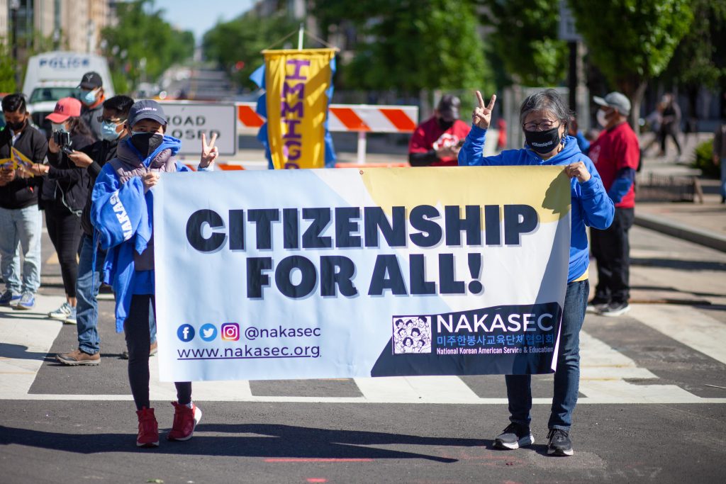 NAKASEC community members hold up a NAKASEC-branded banner that says, "Citizenship For All!" during a rally on the streets of Washington, DC.