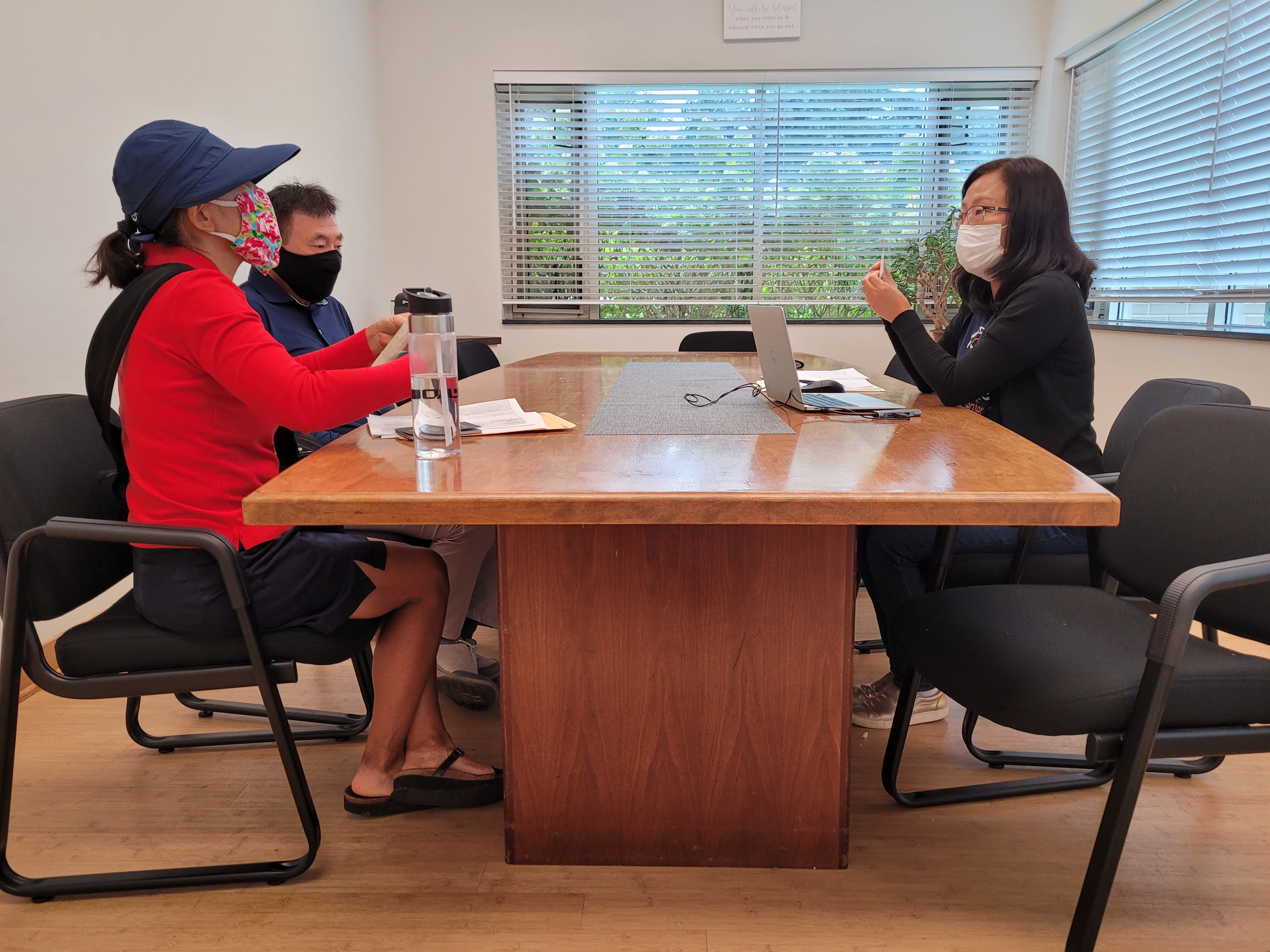 Hamkae Center staff speaks with 2 Korean community members at a table, with papers and a laptop in front of them.