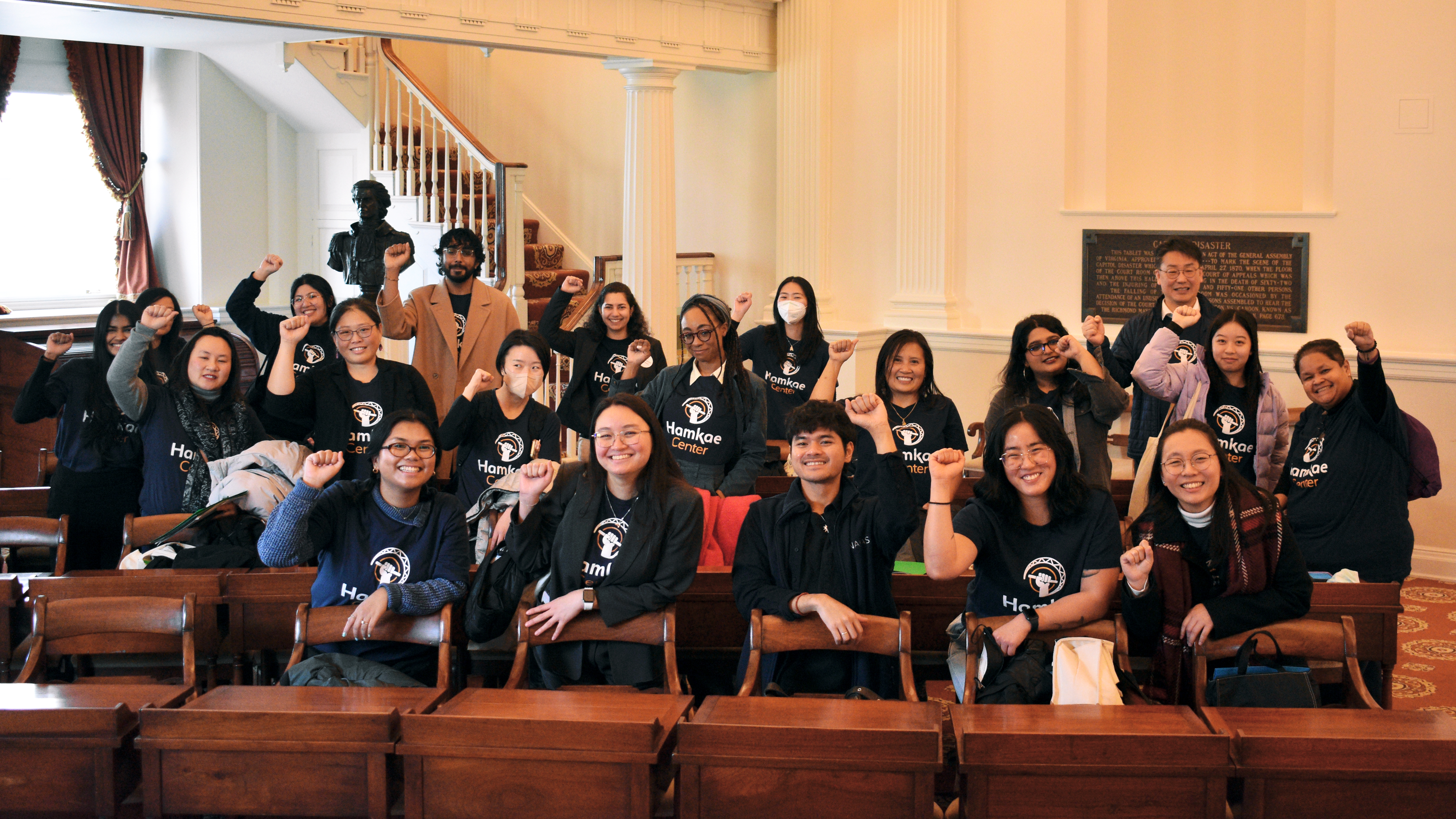 Group photo of Hamkae Center staff and community members holding up a solidarity fist in a room with antique desks at the Virginia General Assembly as part of Hamkae Center's 2025 Advocacy Day.
